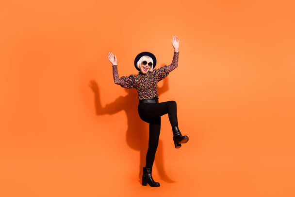 Full size photo of old funky smiling cheerful positive lady in sunglasses dancing raise hands leg isolated on orange color background - Foto, Imagem