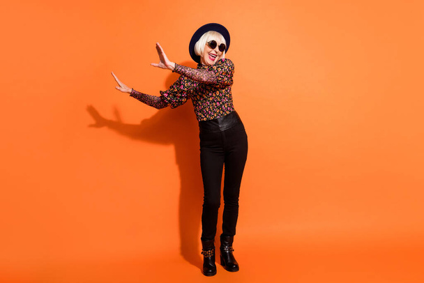 Full size photo of crazy smiling excited happy old lady dancing wear black trousers and glasses isolated on orange color background - Φωτογραφία, εικόνα
