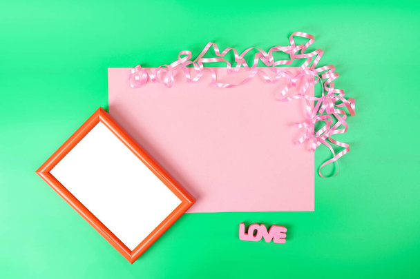 Red photo frame with free space for text on a green background, next to the inscription LOVE and pink copy space. Romantic card for Valentine's Day. - Fotografie, Obrázek