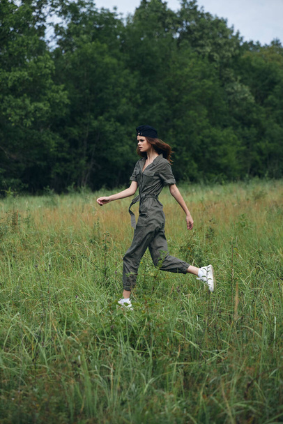 Woman in the field runs on the grass in a green jumpsuit  - Φωτογραφία, εικόνα