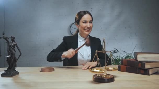 Lächelnder Anwalt mit Hammer in der Nähe der Waage im Büro  - Filmmaterial, Video