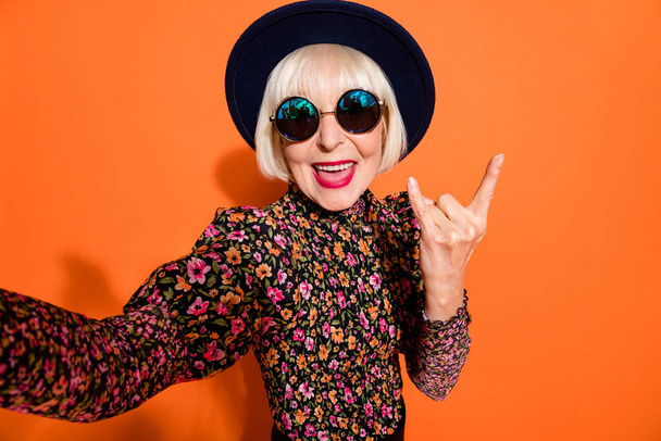 Portrait of old funky crazy smiling good mood lady take selfie showing rock n roll sign isolated on orange color background - 写真・画像
