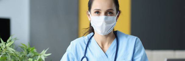 Doctor with protective medical mask siting at table in office and writing in documents - Фото, зображення