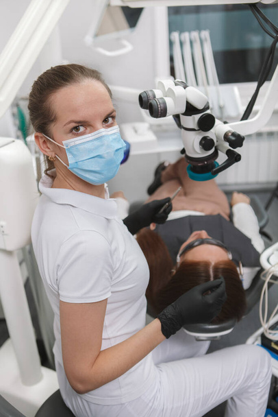 Vertical shot of a professional dentist wearing medical face mask, looking to the camera, while working - Foto, Bild