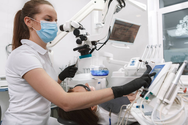 Low angle shot of a professional dentist wearing medical face mask and gloves, using modern automated dental microscope on patient - Foto, immagini