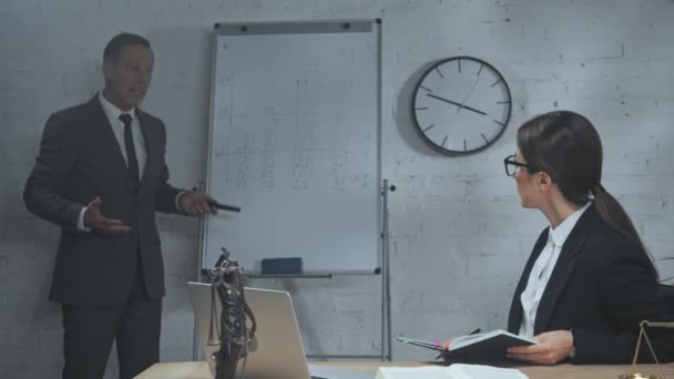 Δικηγόρος δείχνει flipchart κοντά συνάδελφος με σημειωματάριο στο γραφείο  - Πλάνα, βίντεο