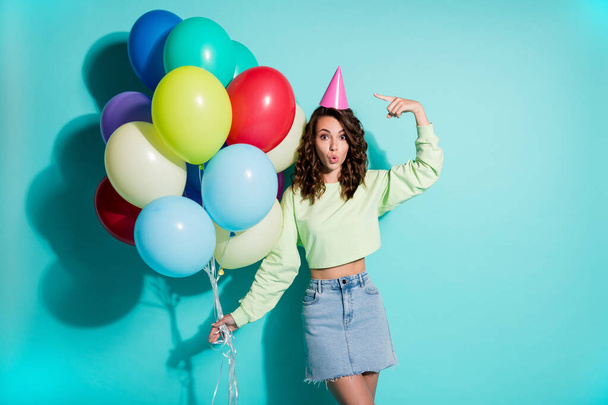 Photo of young lady hold bunch balloons direct finger hat wear cone headwear green sweater jeans short skirt isolated blue color background - Photo, image