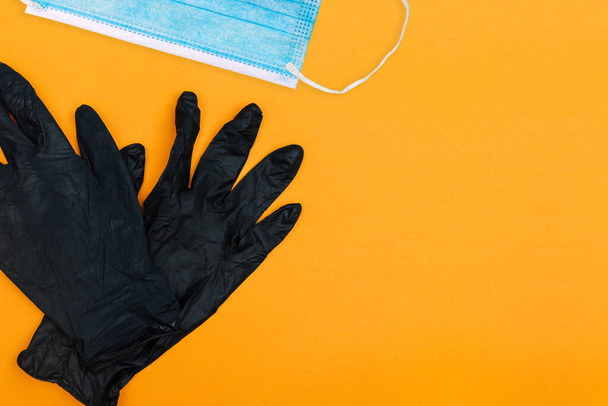 Black gloves with a disposable mask on a colored background. Remedies against coronavirus. Top view with copy space - Photo, Image