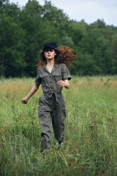 Woman in the field Green jumpsuit black cap jogging on the grass  - Φωτογραφία, εικόνα