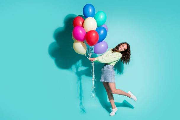 Photo of cute young girl hold many balloons dance wear sneakers green pullover mini jeans skirt isolated blue color background - Fotografie, Obrázek