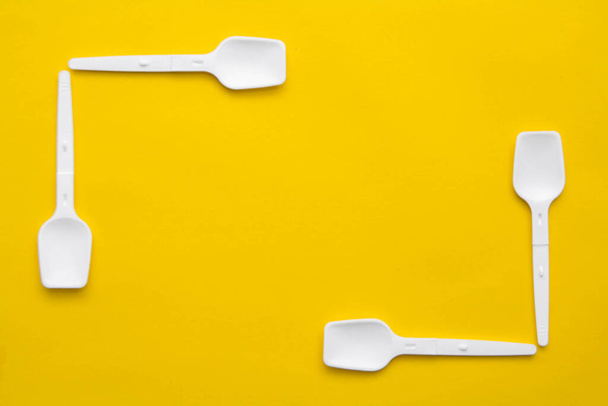 White plastic spoons on yellow background. Fast food, eco and no plastic concept. Top view. Copy, empty space for text. - Фото, изображение