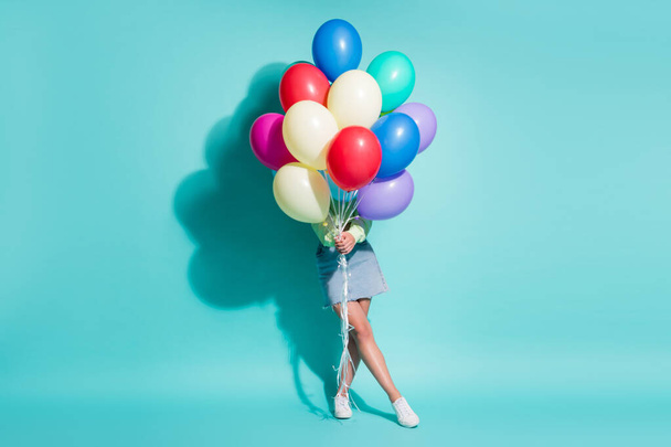 Photo of young lady hold bunch balloons cover herself wear green sweater mini jeans skirt sneakers isolated blue color background - Φωτογραφία, εικόνα