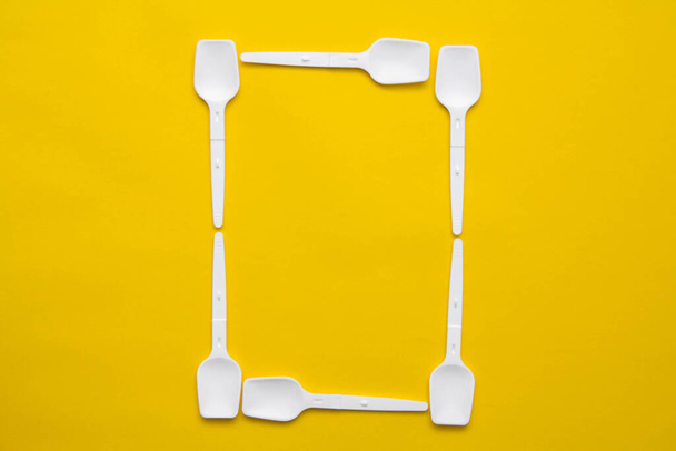 White plastic spoons in the form of letter O on yellow background. Top view. Copy, empty space for text. - Foto, afbeelding