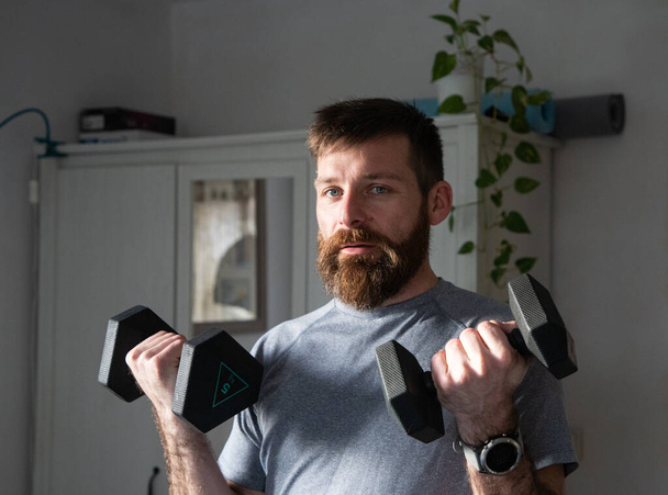 hombre guapo haciendo ejercicio en casa levantando pesas  - Foto, Imagen