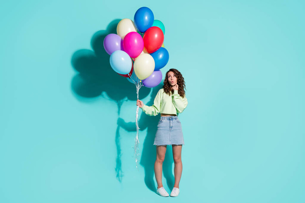 Photo of girl hold many balloons finger cheek look empty space wear green sweater mini jeans skirt sneakers isolated blue color background - Foto, immagini