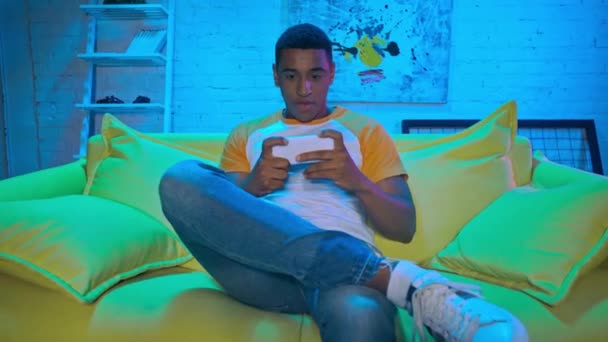 Αφροαμερικάνος παίζει παιχνίδι στο smartphone στο σπίτι  - Πλάνα, βίντεο