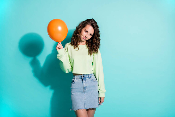 Photo of charming young lady hold small orange balloon wear green pullover denim mini skirt isolated blue color background - Fotografie, Obrázek