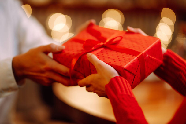 Exchange of gifts. Man gives to his woman surprise a gift box with red ribbon.Young loving couple celebrating Valentines Day. Romantic day. Winter holidays. - 写真・画像