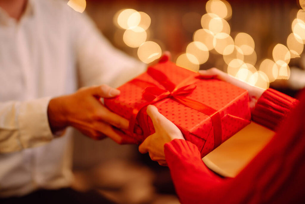 Exchange of gifts. Man gives to his woman surprise a gift box with red ribbon.Young loving couple celebrating Valentines Day. Romantic day. Winter holidays. - Foto, afbeelding