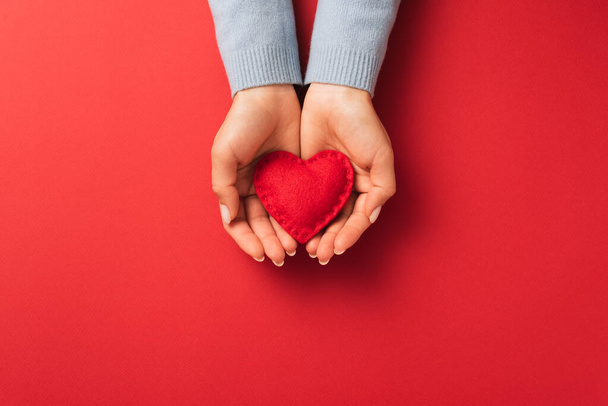Concepto de expresión de amor de San Valentín con corazón rojo en las palmas de las mujeres sobre un fondo rojo - Foto, Imagen