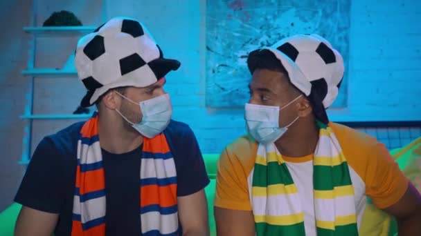 Wieloetniczni fani piłki nożnej w maskach medycznych patrząc mecz - Materiał filmowy, wideo