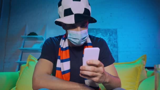 Fotbalový fanoušek v lékařské masce házení smartphone doma  - Záběry, video