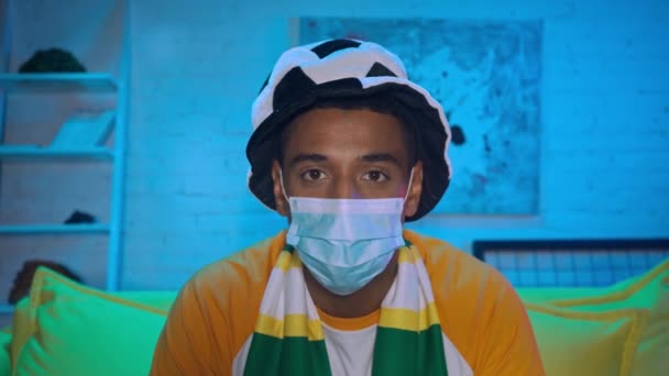 Afrikanischer Fußballfan mit medizinischer Maske blickt in die Kamera  - Filmmaterial, Video