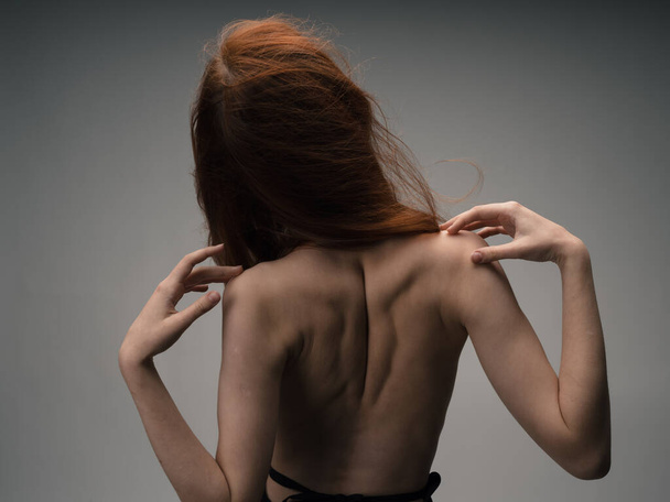 Una sottile donna dai capelli rossi si tocca con le mani dietro la schiena - Foto, immagini