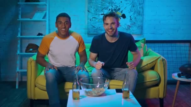 Futbolistas multiétnicos bailando cerca de cerveza y patatas fritas en casa  - Metraje, vídeo