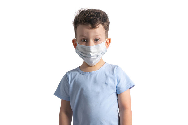 Egy fehér kisfiú orvosi maszkban a koronavírus ellen, fehér alapon. Egy gyerek álarcban vírusoktól és megfázásoktól. Pandémia, járvány, coronovírus, önizoláció. A coronovíruson található anyagok - Fotó, kép