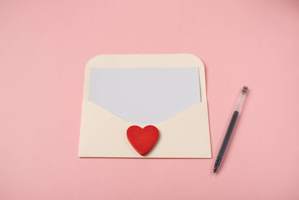 Envelope with a blank sheet of paper inside and red heart on the rose background. Romantic love letter for the Valentine's day concept. Space for text. - Photo, Image