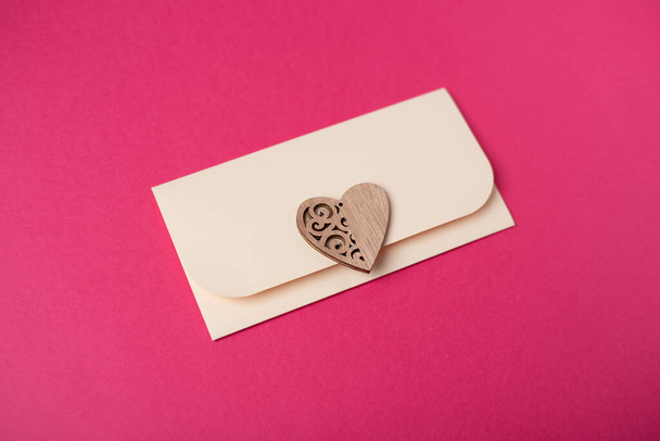 Envelope and wooden heart on the hot pink background. Flat lay. Romantic love letter for Valentine's day concept. - Photo, image
