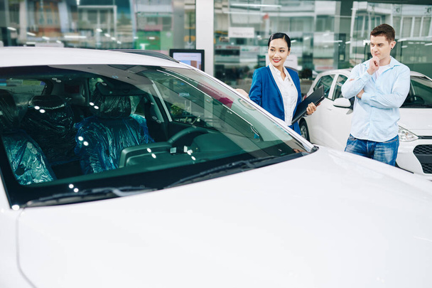 Positiivinen nuori naisautokauppias, joka kutsuu asiakkaan koeajelemaan autoa - Valokuva, kuva