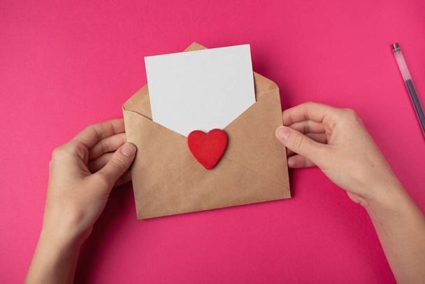 Woman's hands holding a letter in craft envelope on the hot pink background. Valentine's day concept. Space for text. - Photo, Image