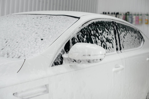 Modern washing with foam and high-pressure water of a white car. Car wash - 写真・画像