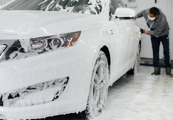 Μοντέρνο πλύσιμο με αφρό και νερό υψηλής πίεσης ενός λευκού αυτοκινήτου. Πλύσιμο αυτοκινήτου - Φωτογραφία, εικόνα