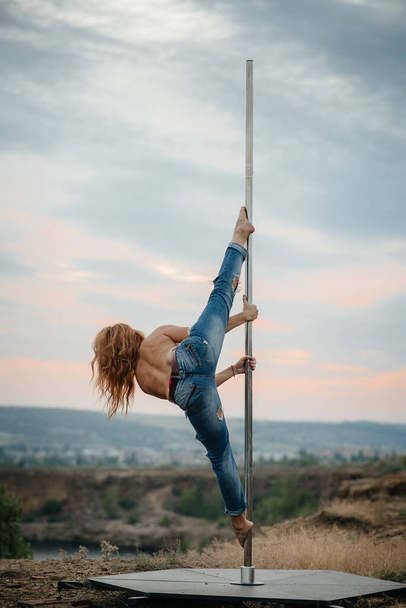 A young sexy girl performs amazing exercises on a pole during a beautiful sunset. Dance. Sexuality - Foto, immagini