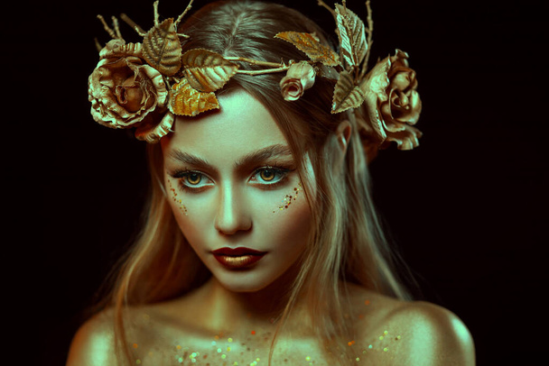 Fantasy portrait of woman with golden skin. Girl goddess in wreath, gold roses, accessories. Beautiful face, steel glitter makeup. Artistic photo, black background. Elf fairy princess. Fashion model. - Fotoğraf, Görsel