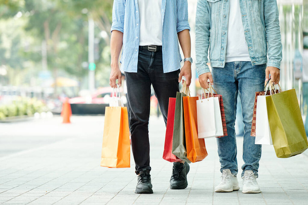 Imagen recortada de hombres jóvenes caminando por la calle con muchas bolsas de compras en las manos - Foto, imagen