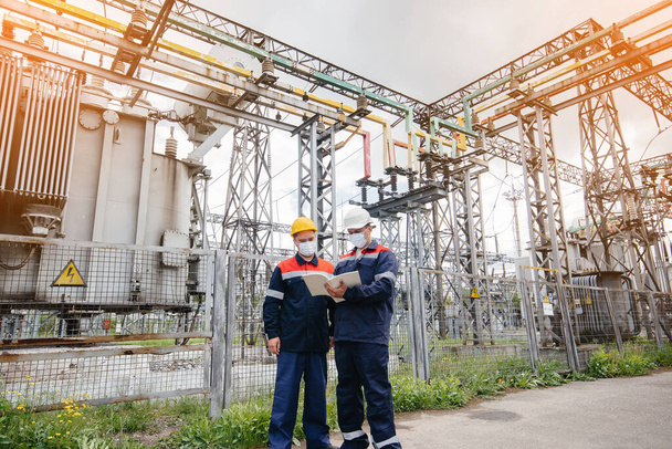 Engineers electrical substations conduct a survey of modern high-voltage equipment in the mask at the time of pandemia in the evening. Energy. Industry - Foto, imagen
