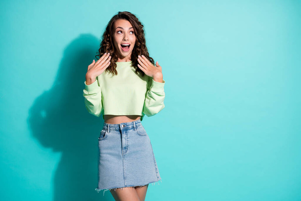 Portrait of surprised curly young woman dressed casualwear raise hands look empty space isolated on turquoise color background - Foto, Bild