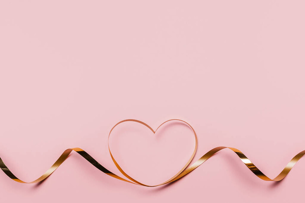 shape heart by gold ribbon on isolated pink background - Foto, Bild