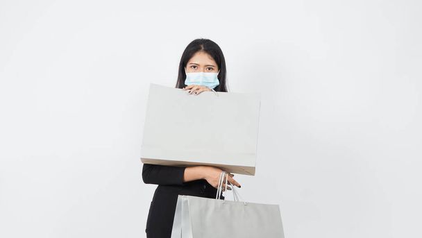Covid 19 en winkelconcept. Aziatische vrouw draagt gezichtsmasker hold boodschappentas. Meisje en papieren zak vertegenwoordigen winkelen tijdens coronavirus crisis of covid19 uitbraak. shopper en virus masker. wit B - Foto, afbeelding
