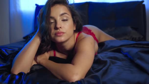 mujer sexy tocando el cabello y mirando a la cámara en la ropa de cama de satén negro - Metraje, vídeo