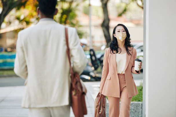 Assez grave jeune femme d'affaires asiatique en masque de protection va travailler le matin avec prendre le café dans les mains - Photo, image