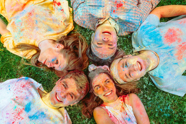 счастливые друзья, лежащие на зеленой траве, испачканные в цвета оли. Индийский праздник - Фото, изображение