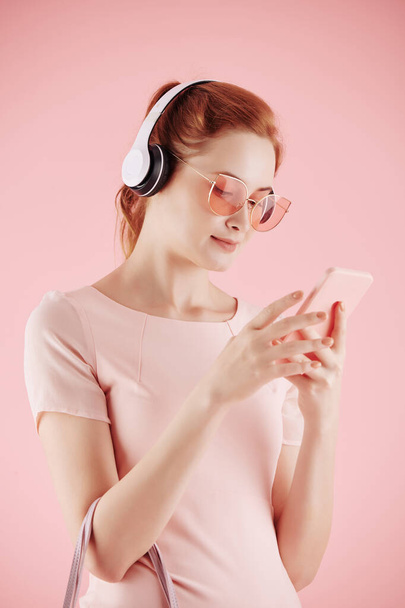 Mosolygó fiatal csinos nő fülhallgató hallgat zenét az ő smartphone - Fotó, kép