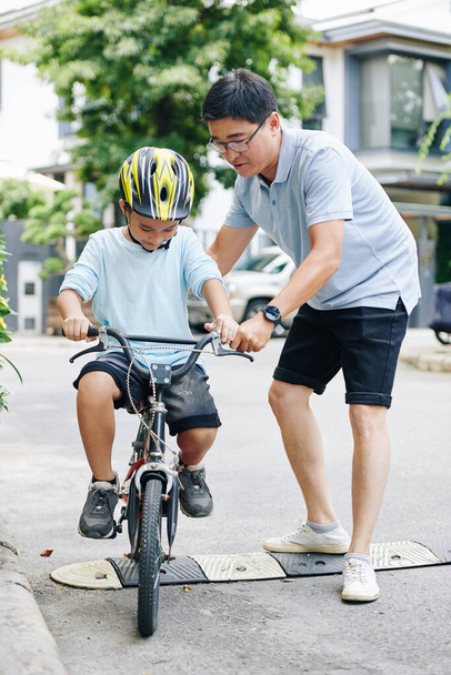 Padre ayudando a hijo preadolescente que montar en bicicleta por primera vez - Foto, Imagen