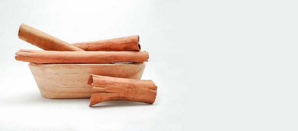 Cynamonowa kora (Cinnamomum zeylanicum lub Cinnamomum verum) w drewnianej misce na białym tle z przestrzenią do kopiowania - Zdjęcie, obraz