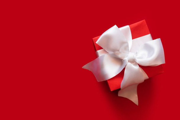 Piros ajándék doboz fehér szalaggal a piros színű háttér. - Fotó, kép